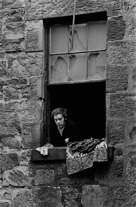 photograph of a man looking out the window of a derilict building